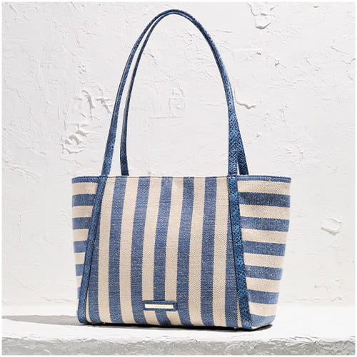 Blue and white striped woven tote bag with leather handles, displayed against a textured white wall.