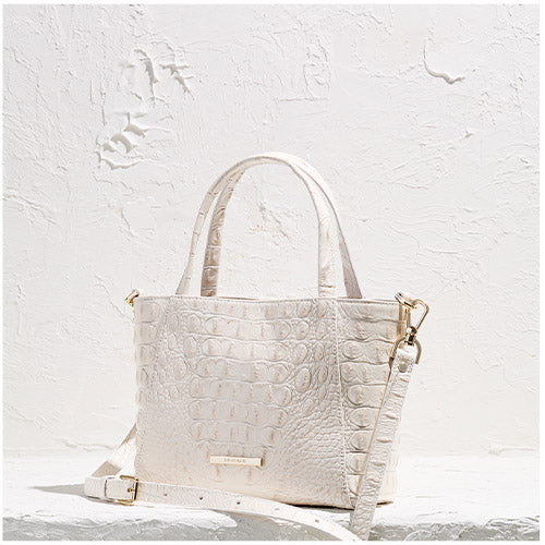 White croc textured handbag with gold accents on a light gray background