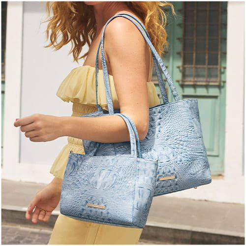 Light blue crocodile-embossed leather tote and matching mini bag carried together by a model.