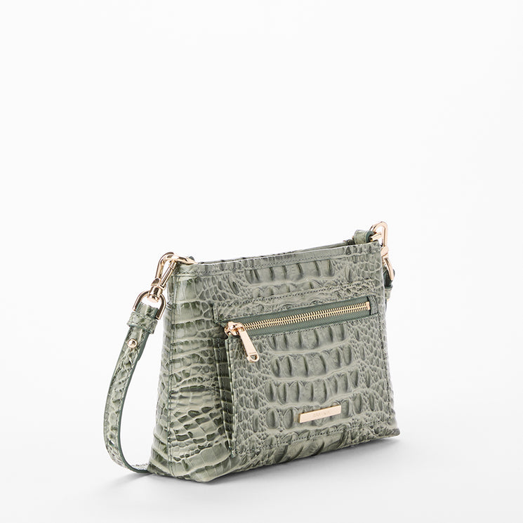 A sage green crocodile-embossed leather crossbody handbag with a front zippered pocket and a small gold-tone logo plate, shown on a clean white background. Side view.