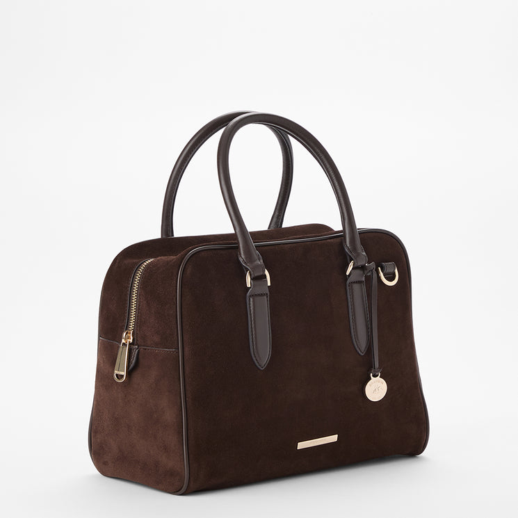 A dark brown suede handbag with dark brown leather handles, gold-tone hardware, and a small round metal charm, shown on a clean white background.