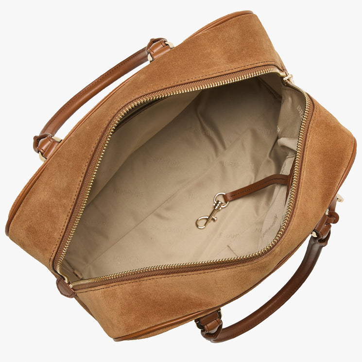 A tan suede bag shown open from an overhead angle, revealing a beige interior lining and brown leather handles on a plain white background.