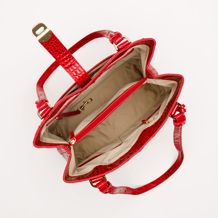 Top-down view of a red Brahmin Fiora bucket bag featuring a glossy embossed texture, gold-tone hardware, two straps, and a beige fabric-lined interior with a center zippered compartment and side pockets.