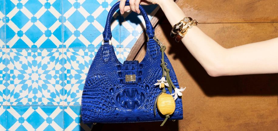 Blue handbag with floral details held by a hand against a blue and white patterned wall.