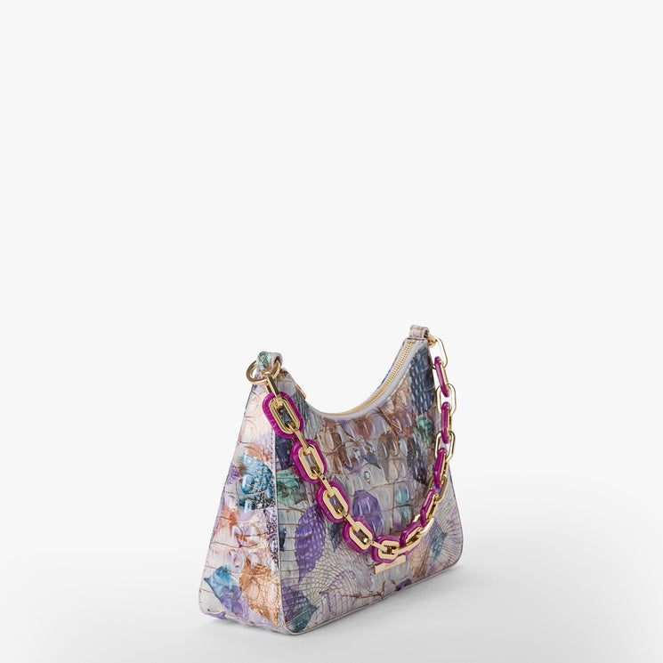 Brahmin floral handbag with pastel print, structured trapezoid silhouette, glossy textured finish, and chunky gold and pink chain strap. Displayed on white background; front and top views visible.