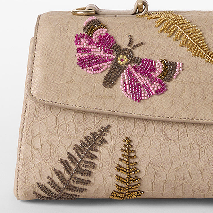 Beige handbag with butterfly and fern designs on a white background. Dayan close up.
