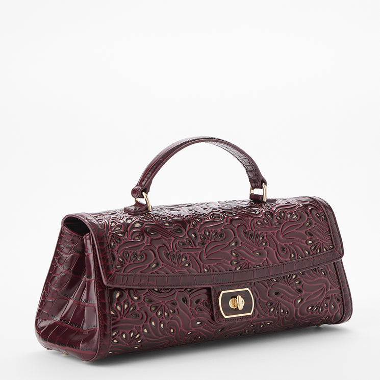 A burgundy embossed leather handbag with a top handle, featuring an intricate floral cutout pattern and a gold-tone turn-lock closure on the front flap, set against a plain white background.