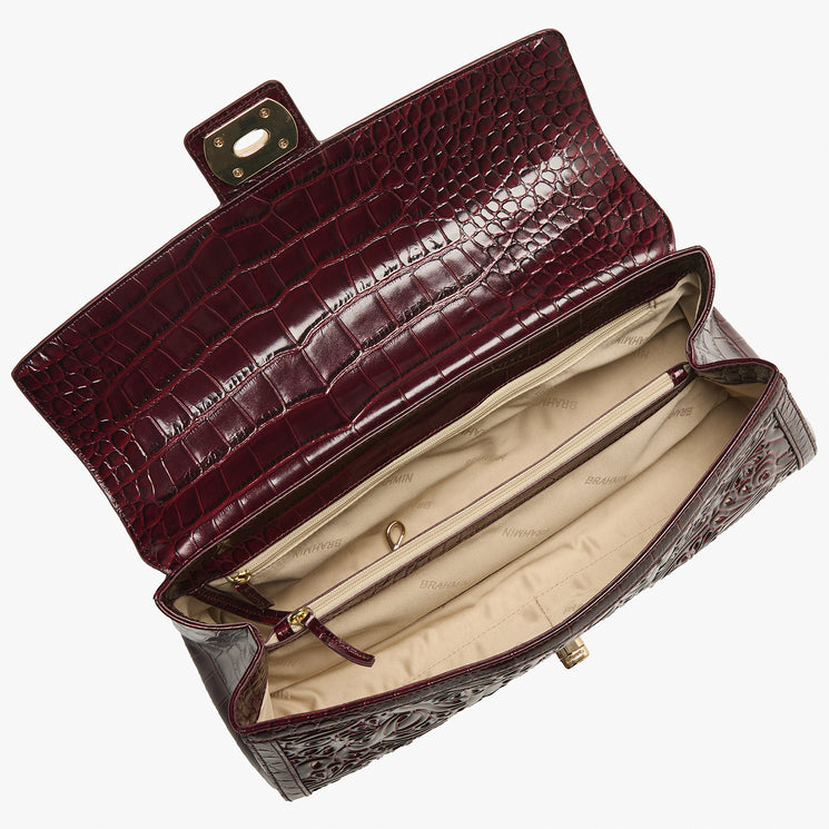 A luxury crocodile-embossed clutch bag in deep burgundy, shown open to reveal a beige interior lining and gold-tone hardware, set against a plain white background.