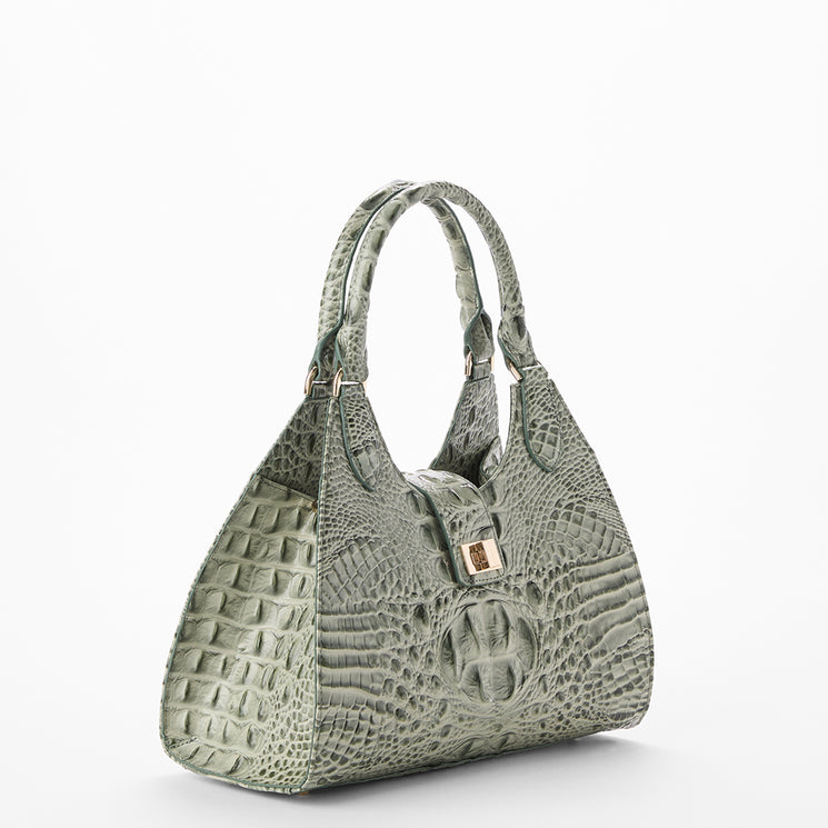 A structured shoulder bag with a crocodile-embossed texture in a muted sage green color, featuring dual top handles and a small gold-tone clasp on the front, set against a plain white background.