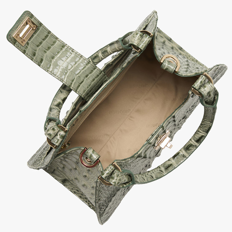 An open sage green crocodile-embossed handbag with gold-tone hardware, shown from a top-down perspective against a light gray background.