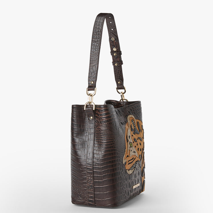 Side view of a Brahmin handbag in dark brown with embossed textured pattern, large embroidered animal face on front, gold-tone hardware, adjustable shoulder strap, structured silhouette.