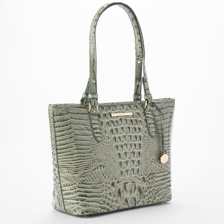 A sage green crocodile-embossed leather tote bag with dual shoulder straps, gold-tone hardware, and a small hanging round charm, shown on a plain white background.