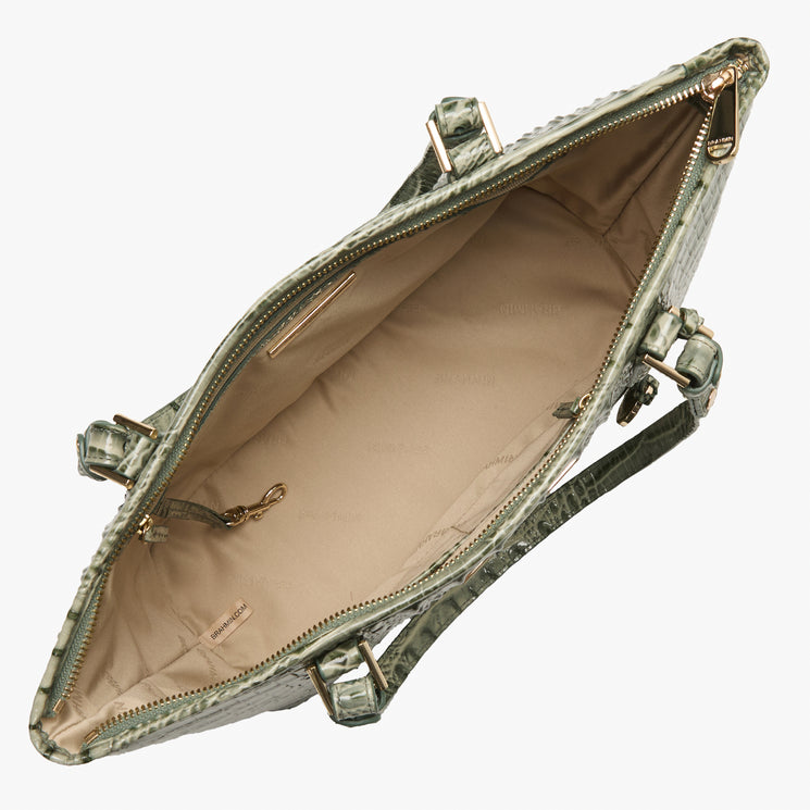 An open handbag with a textured green patterned exterior, showing a beige interior lining and gold-tone hardware, photographed on a light gray background.