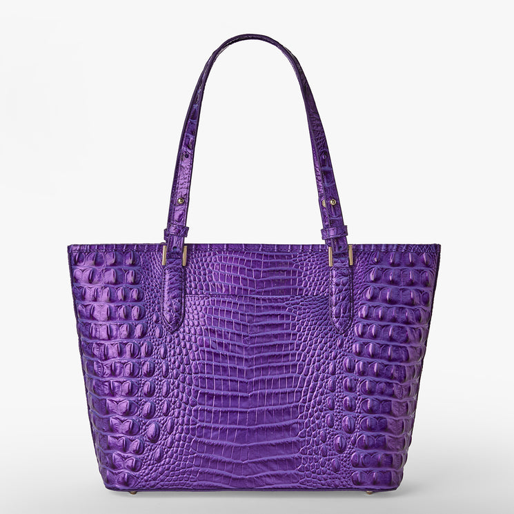 Brahmin purple tote bag with an embossed textured pattern, two top handles, structured silhouette, gold-tone hardware, and a spacious interior, shown upright against a white background.