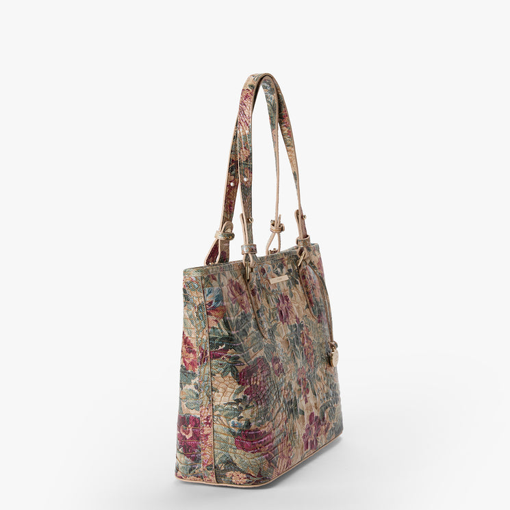 A structured tote bag with a dense floral and botanical pattern in muted tones of green, burgundy, and beige, featuring dual shoulder straps and gold-tone hardware, shown against a plain white background.