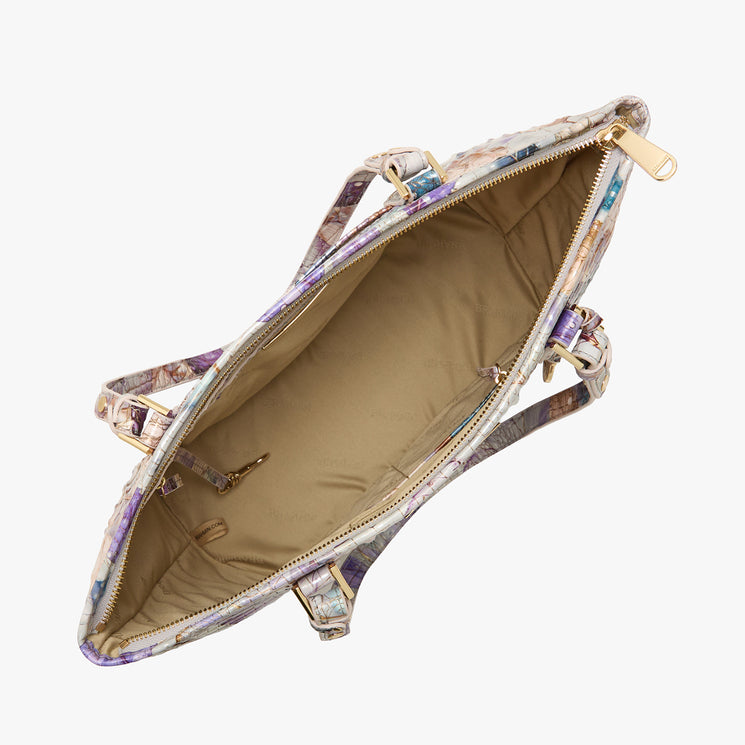Top view of an open Brahmin floral satchel featuring beige lining, gold zipper hardware, dual interior pockets, spacious main compartment, and a colorful patterned exterior. Adjustable shoulder strap partially visible.
