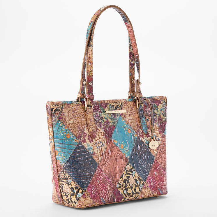 Brahmin patchwork tote bag in multicolor with floral, reptile-embossed, and abstract textured panels, double top handles, gold-tone logo charm, and structured silhouette. Front view shows exterior details.