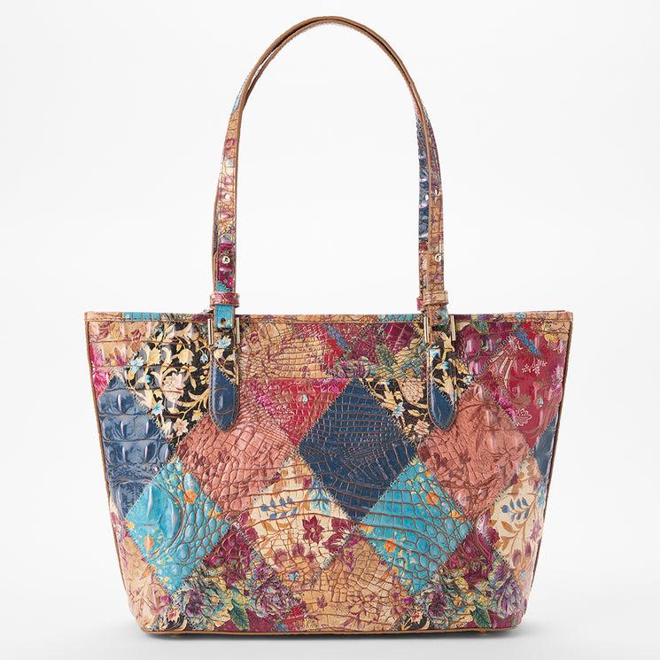 Brahmin tote bag with two handles and gold-tone hardware, showcasing a colorful patchwork design in blue, red, pink, tan, and gold with embossed textures and floral, animal-inspired, and geometric patterns.