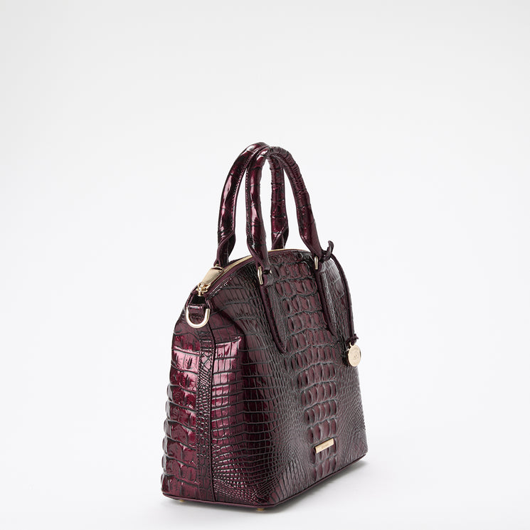 A structured satchel handbag with a glossy embossed crocodile pattern in deep burgundy, featuring dual top handles, gold-tone hardware, and a small gold brand plaque on a clean white background.