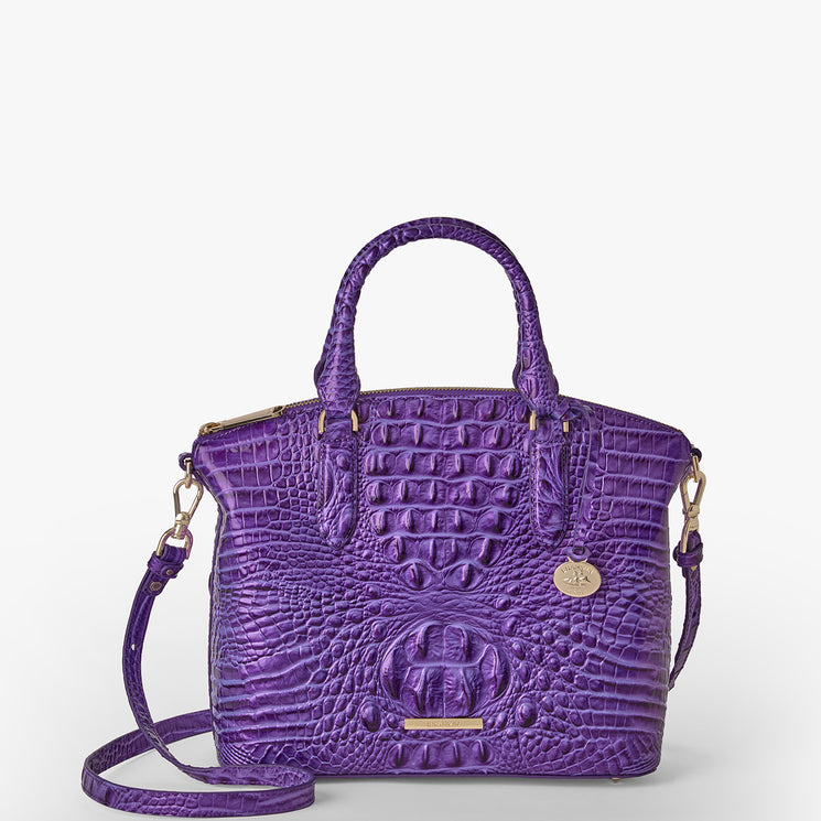 Brahmin handbag in rich purple with embossed textured pattern, gold hardware, structured top handle, detachable shoulder strap, round gold charm; shown on a white background.