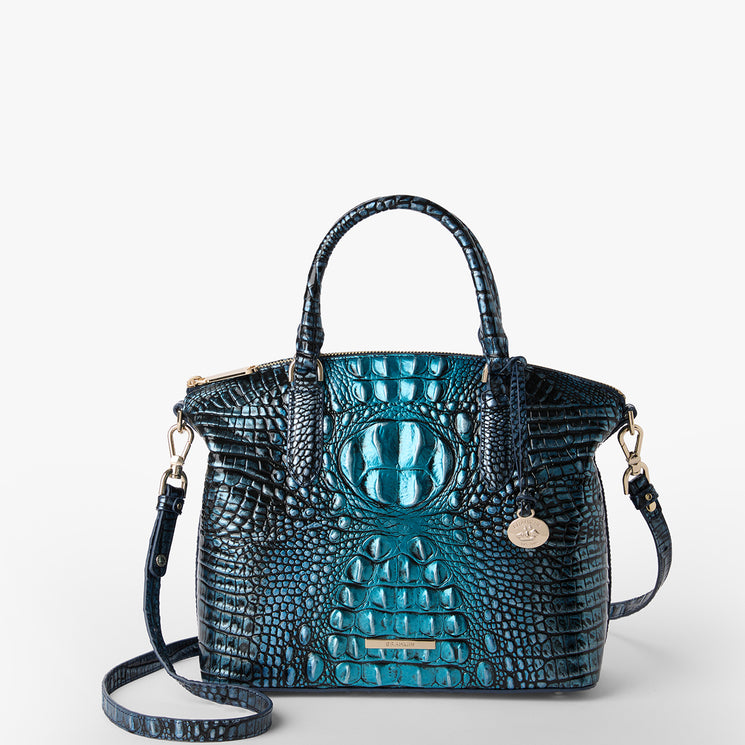 Brahmin structured satchel in shiny teal and navy with embossed texture, gold hardware, two top handles, detachable shoulder strap, round gold logo charm; elegant shape shown from front three-quarter view.