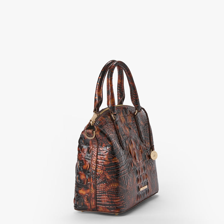 A brown textured handbag with a crocodile skin pattern, featuring dual top handles, gold-tone hardware, and a small round charm, shown against a plain white background.