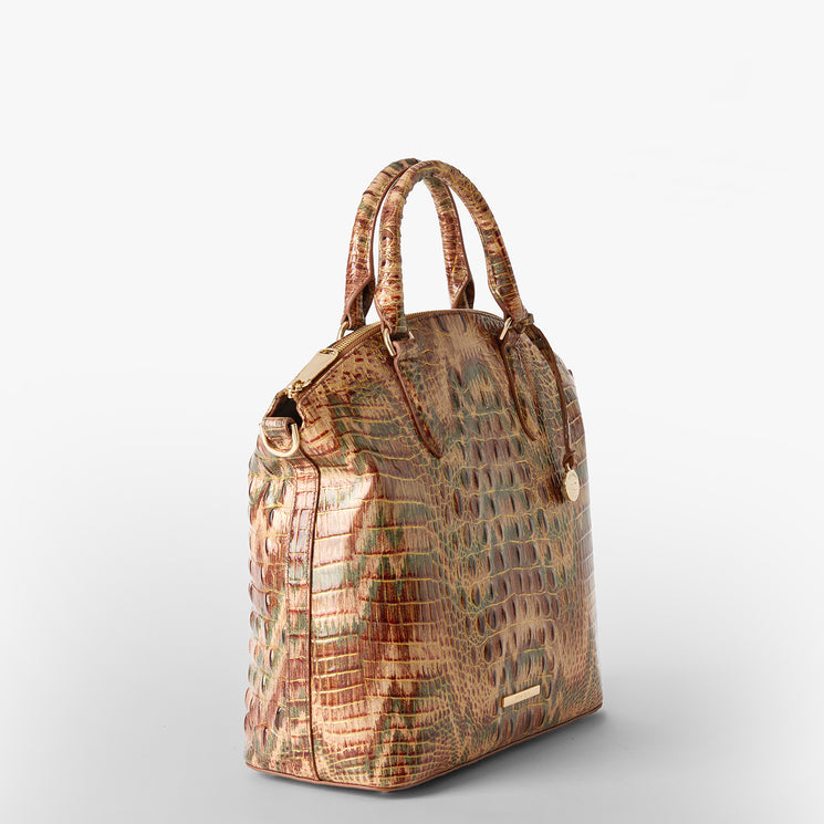 A structured handbag with a crocodile-embossed texture in earthy brown, beige, and muted green tones, featuring dual top handles and a gold Brahmin logo plaque. Large Duxbury Satchel Side View.