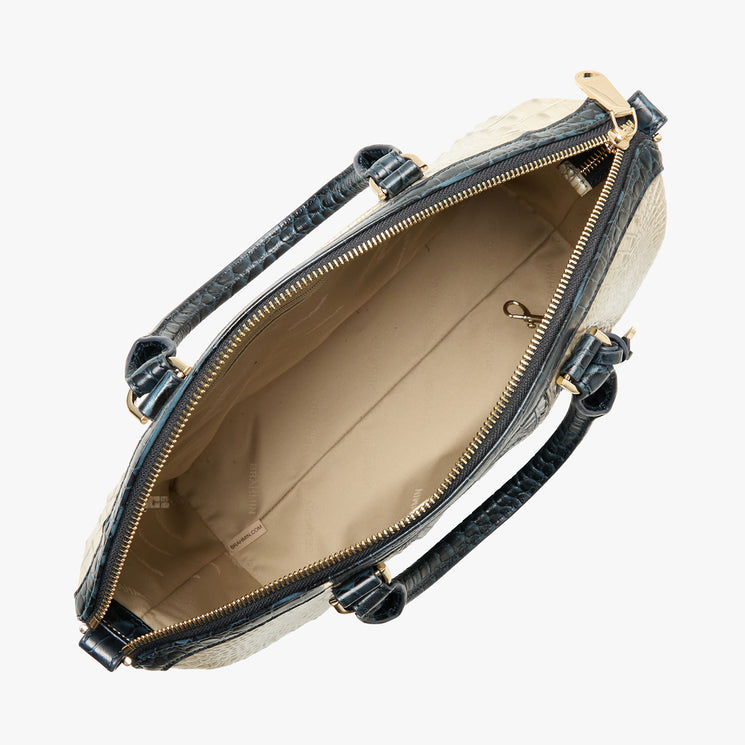 Top view of Brahmin satchel with cream and dark embossed exterior, gold-tone zipper, two black textured handles, beige-lined interior, small gold clasp inside, and structured silhouette.