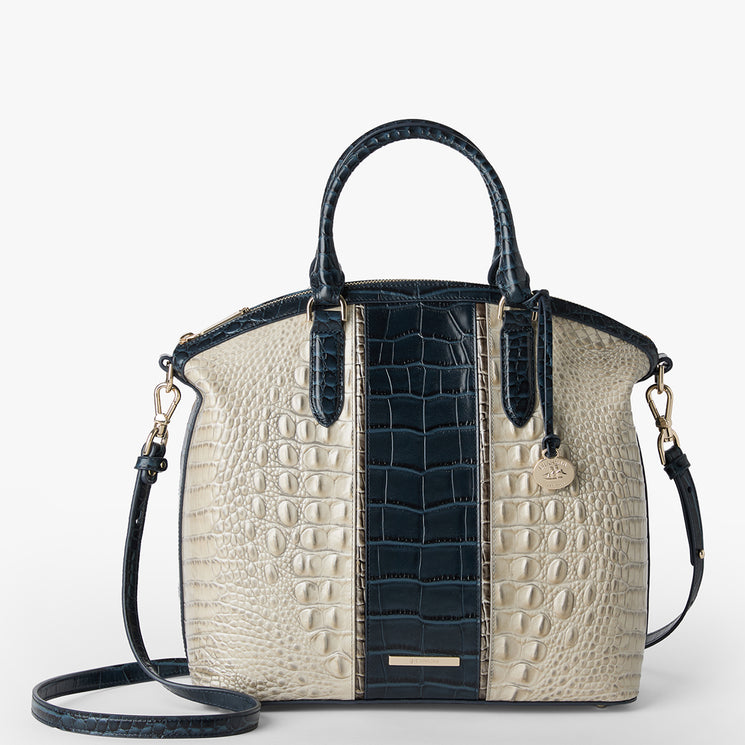 Brahmin handbag in a dark blue and cream embossed texture, structured silhouette with two top handles, adjustable crossbody strap, gold-tone hardware, round logo charm; displayed on a white background.