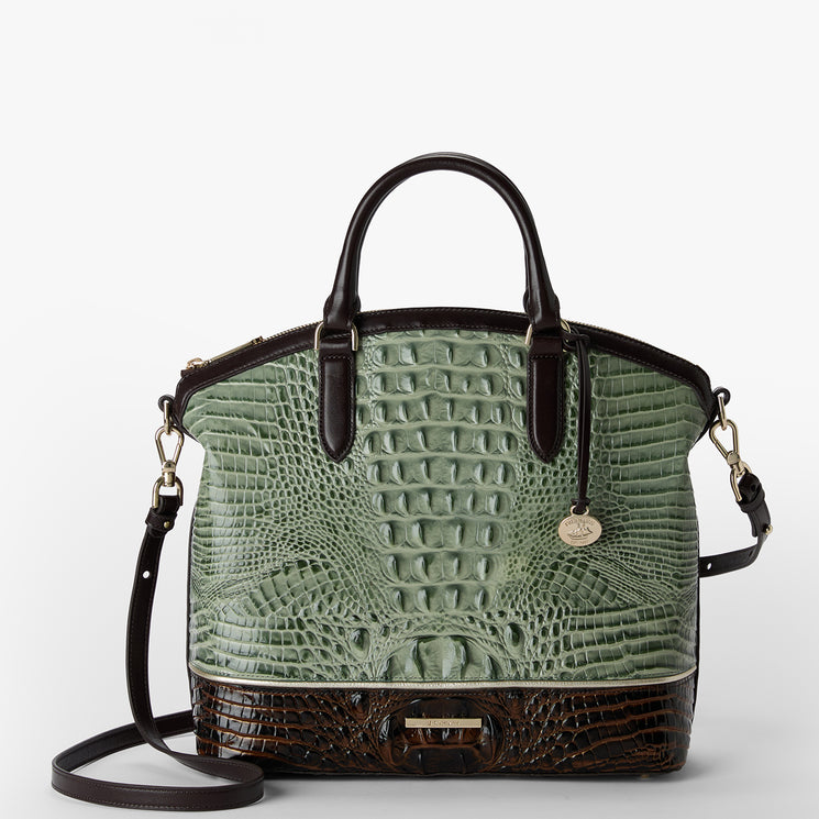 A structured handbag with a light sage green crocodile-embossed front and dark brown leather trim, handles, and base, featuring a gold-tone hanging logo charm.