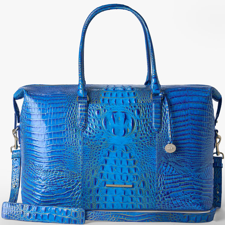 Brahmin bright blue embossed handbag with double handles, a detachable shoulder strap, gold-tone hardware, and a small round charm on the side. Structured silhouette with textured pattern. Front view.