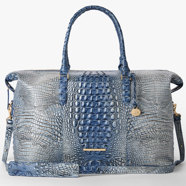 Brahmin blue and gray satchel handbag with embossed texture, dual top handles, long adjustable shoulder strap, gold-tone hardware and charm, shown on a plain white background.