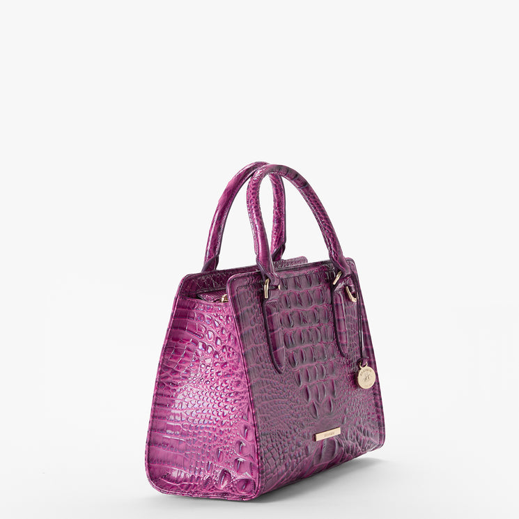 Brahmin handbag in a purple textured embossed pattern, featuring double handles, gold-tone hardware, signature logo charm, and structured silhouette. Shown on a plain white background, exterior details are visible.