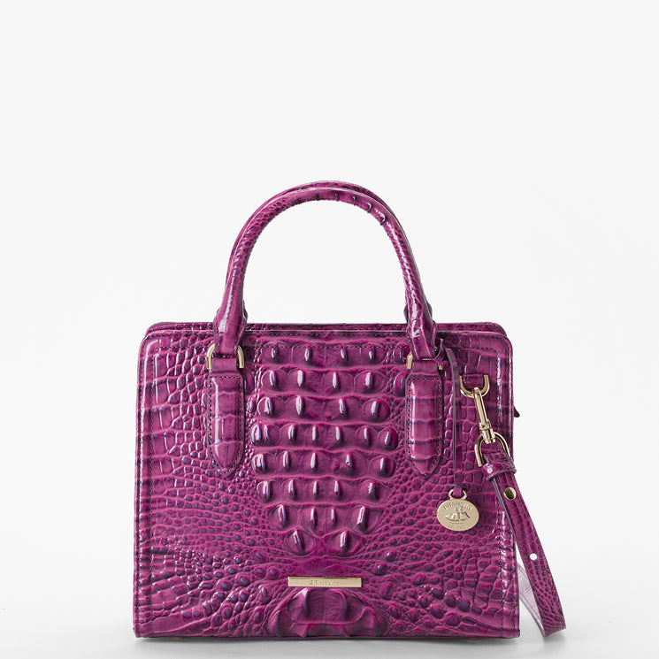 Brahmin square purple handbag with embossed texture, two top handles, gold-tone hardware, detachable shoulder strap, and round gold charm. Set against a white background. No interior details visible.