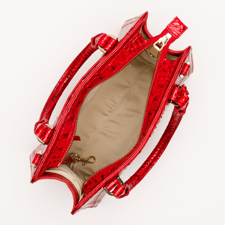 Top-down view of a bright red, croc-embossed Brahmin Cami satchel featuring rolled top handles, gold-tone hardware, and an open, fabric-lined interior with a lobster clasp tether.