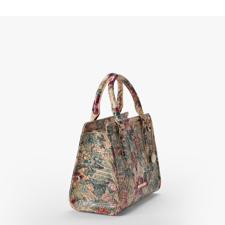 A structured handbag with a multicolor floral pattern, featuring dual top handles and a small gold-tone Brahmin plaque on the front, set against a plain white background.