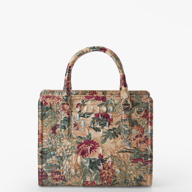 A structured tote bag featuring an intricate floral tapestry pattern in muted red, green, beige, and blue tones, with two top handles and a back pocket, shown against a plain white background.