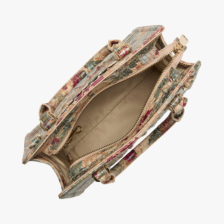 An open handbag with a vintage floral tapestry pattern in muted red, green, and beige tones, showing its beige interior lining and gold-tone hardware against a light gray background.