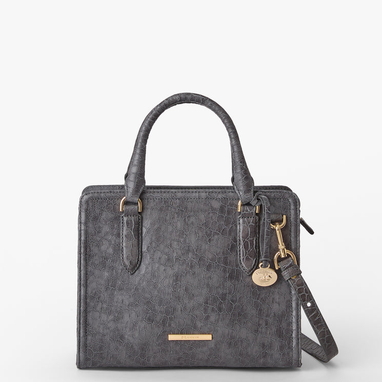 Brahmin grey handbag with textured finish, structured silhouette, dual top handles, detachable shoulder strap, gold-tone hardware accents including a round charm and nameplate. Displayed against a white background.