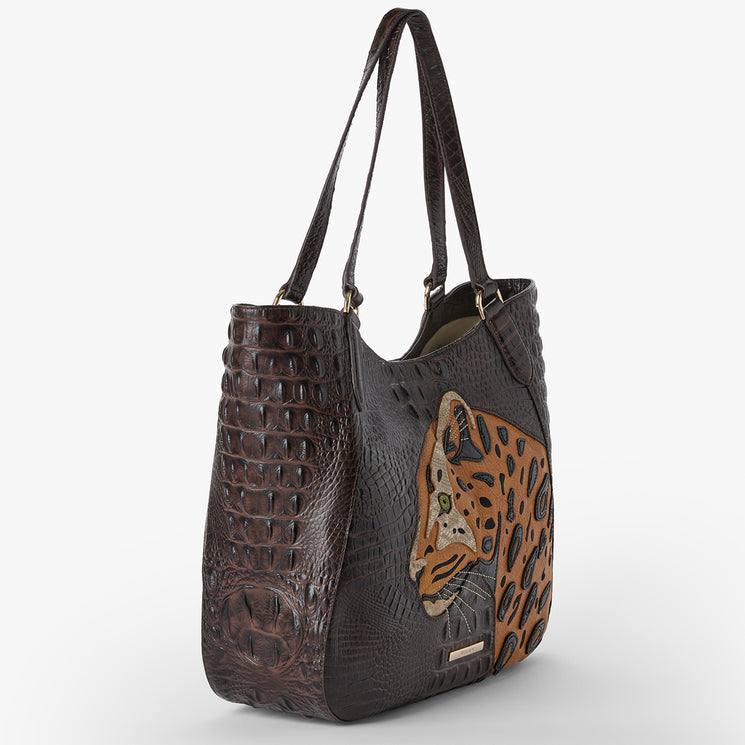 Brahmin dark brown tote bag featuring embossed textured surface, two top handles, embroidered animal-inspired face detail on the side, structured silhouette, light-colored interior, and open top.