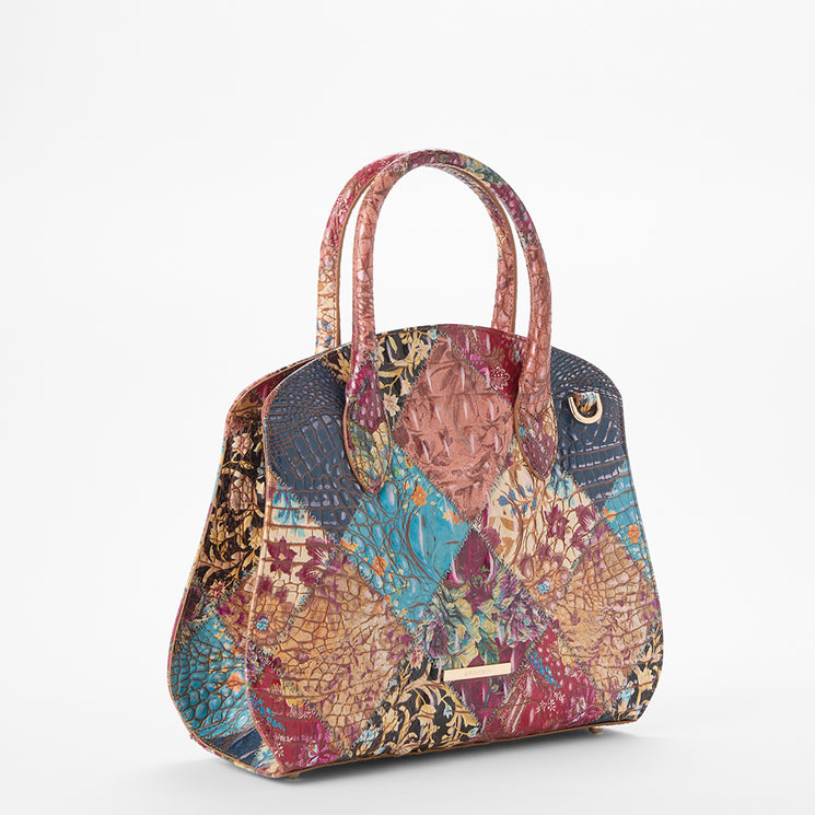 Brahmin patchwork satchel with double handles, showcases textured patterns in pink, blue, yellow, and brown panels. Set on a white backdrop. Structured silhouette; top-handle style displayed from the front.