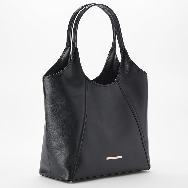 Brahmin black tote bag with curved seam details, double top handles, rectangular metal logo plate at the lower front, smooth texture, structured silhouette, set against a white background.
