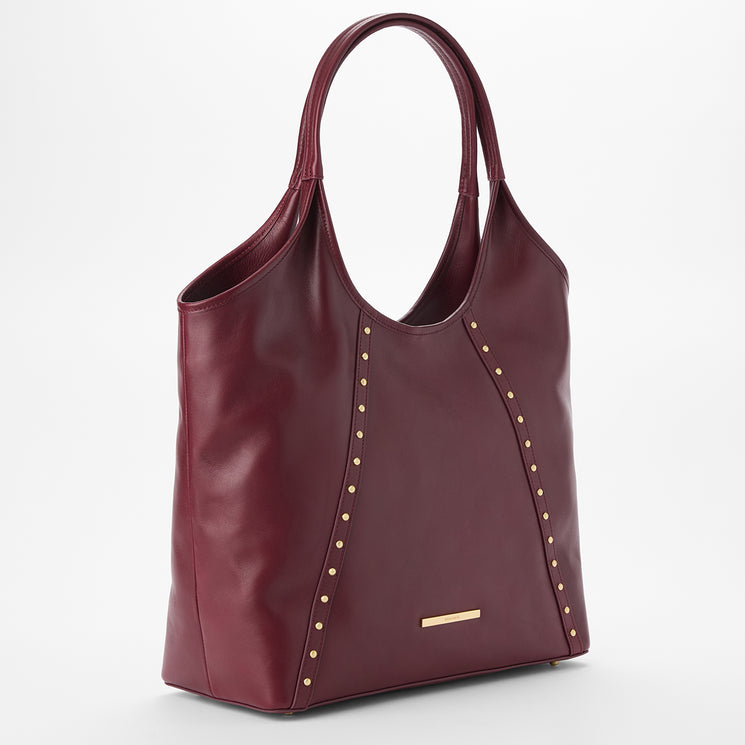 Brahmin burgundy leather tote bag with gold-tone studs along curved seams, gold rectangular logo plate on the front, dual top handles, structured silhouette. Shown on a white background.