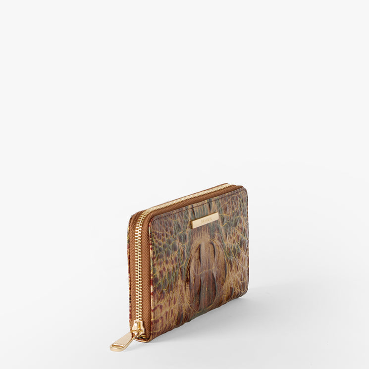A zip-around wallet with a textured crocodile skin pattern in brown, beige, and green, featuring a gold Brahmin plaque and zipper pull. Suri Side View.