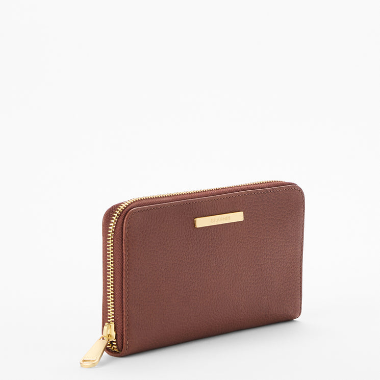 Brahmin brown zippered wallet with gold-tone hardware, including a gold zipper and front nameplate, shown on a plain white background. Smooth texture and compact silhouette are visible.